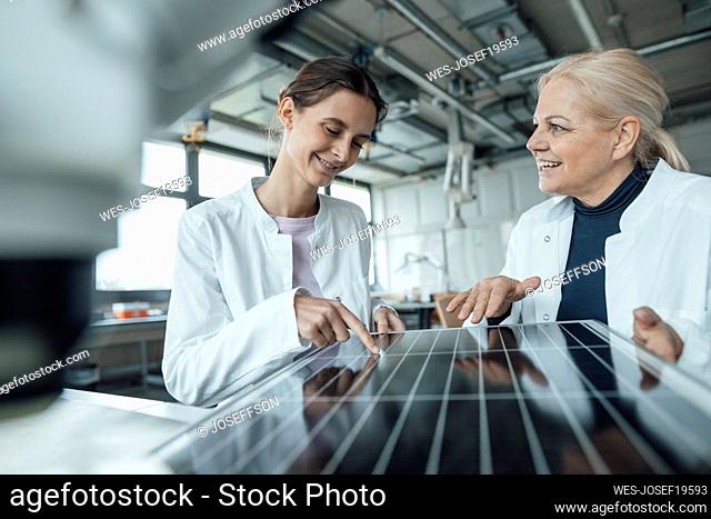 Happy scientists discussing over solar panel in laboratory