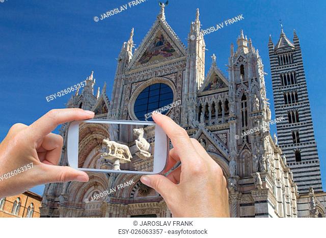In the bottom left of the photo are hands holding smart phone and taking picture of Siena Cathedral and detail of sculpture of the wolf