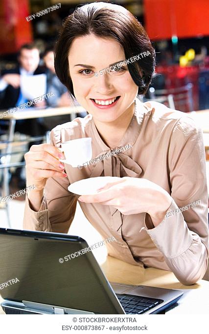 Portrait of businesswoman in the cafe with cup of coffee in hands and laptop near by on the background of sitting men