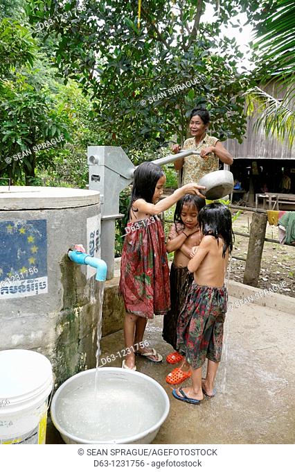 CAMBODIA. Sorn Thong Pin 55 using hand pump to get water from her well, while her grandaughters Chenda 6, San Samey 7 and Chanthou 9 take a bath, Sesan village