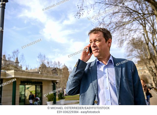 A middle age businessman standing in a park while talking on his phone