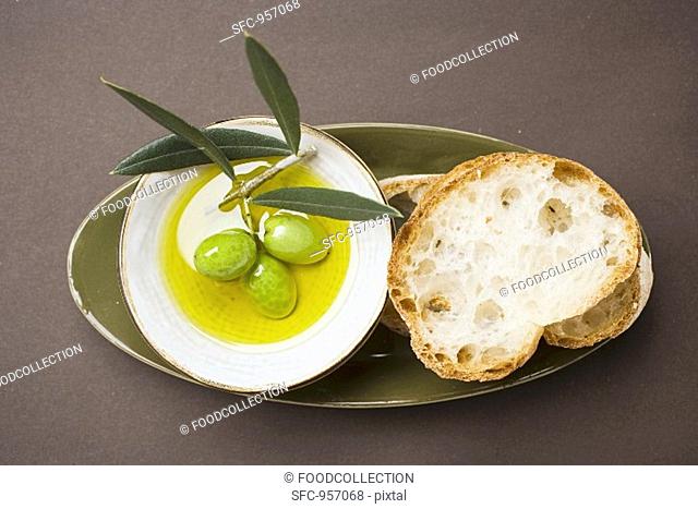 Green olives on twig in bowl of olive oil, white bread