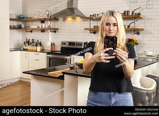 A young Caucasian woman taking selfie in her home kitchen