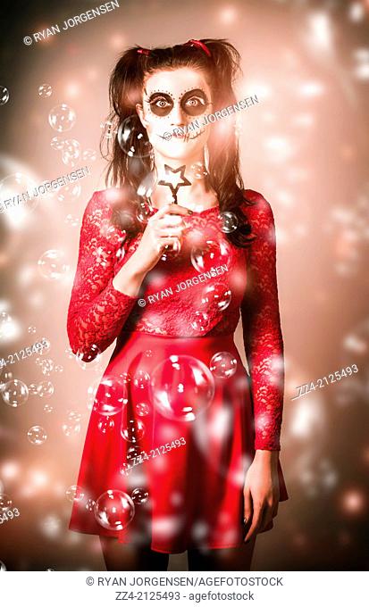 Scary horror photo of a voodoo girl with skeleton make-up blowing soap bubbles to celebrate the deceased during the Mexican horror festival Day of the Dead or...