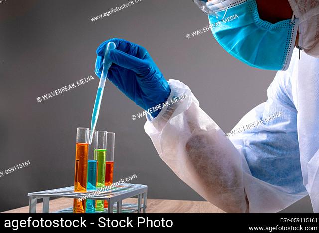 Mid section of health worker wearing face mask working with chemicals in test tubes
