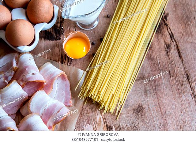Ingredients for Pasta Carbonara with bacon, cheese, cream and yolk on wooden table. Preparing Spaghetti alla carbonara