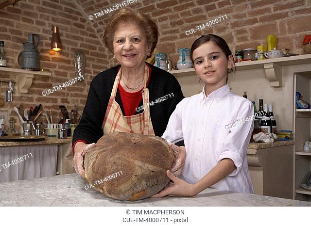Senior woman and granddaughter 9-11 holding loaf, portrait