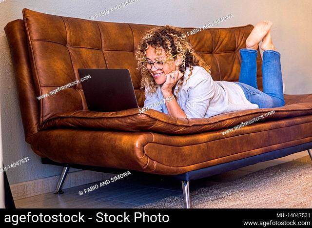 adult woman lay down on te sofa and use laptop computer smiling and having fun alone at home - people female and internet online web surfing activity - cheerful...