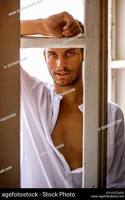 Portrait of handsome young man with beard entering the room with wooden doors