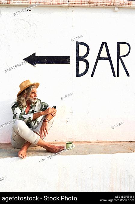 Man wearing hat sitting on retaining wall