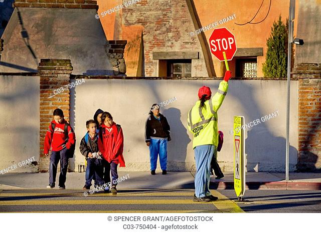 A Hispanic school crossing guard with a 'Stop' sign controls street traffic as Southern California elementary school students and parents arrive in the morning