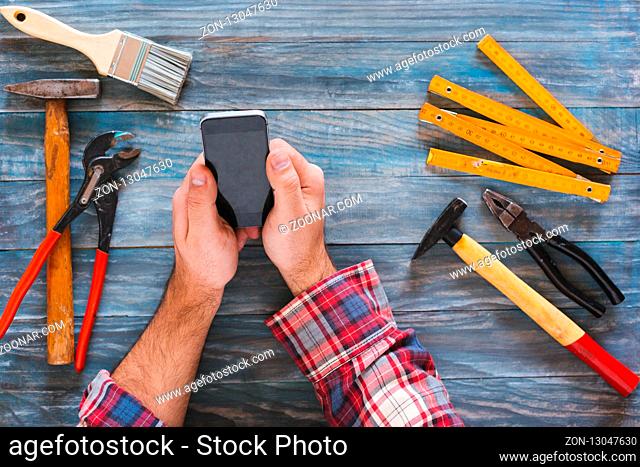 Man working on a DIY project with his phone, wood shavings and carpentry tools and construction all around, top view