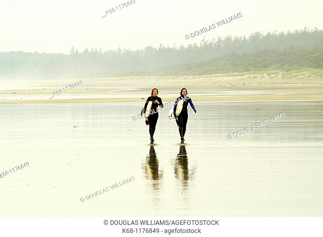 two female surfers carry surfboards on the beach near Tofino, British Columbia, Canada
