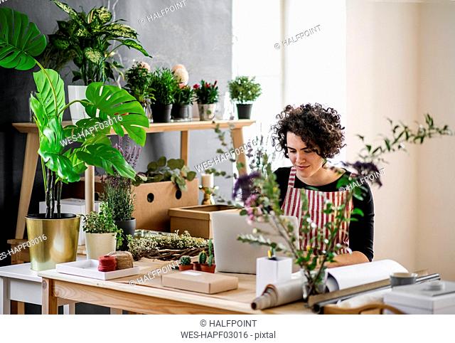 Young woman using laptop in a small shop with plants