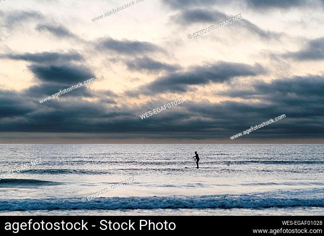 Female paddleboarder surfing on sea during dawn