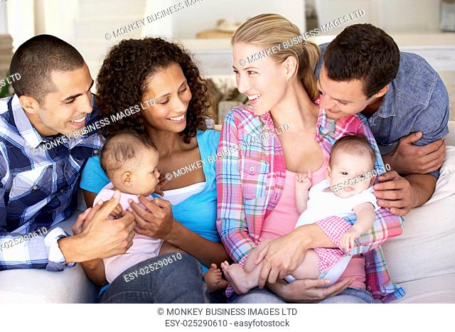 Two Young Family With Babies On Sofa At Home