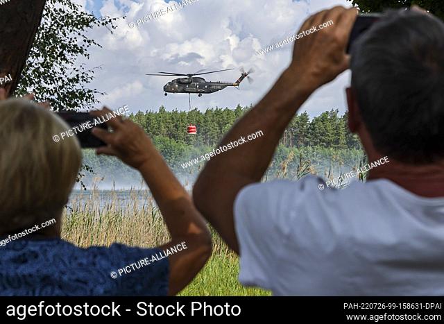 26 July 2022, Brandenburg, Falkenberg: A Bell CH-53 Bundeswehr helicopter fetches firefighting water from the Kiebitz dredging pond to fight the forest fire