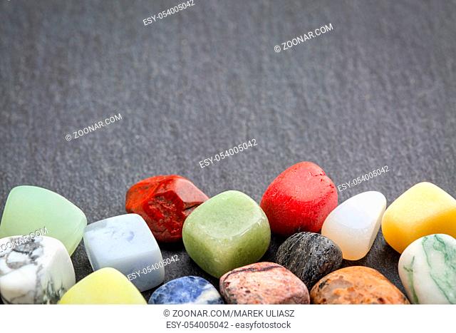 polished, semiprecious, colorful gemstones against gray slate stone with a copy space