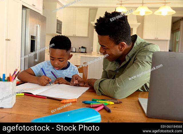 Happy african american father with son doing homework at home smiling