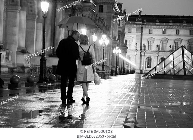 Caucasian couple kissing in rain at night at the Louvre