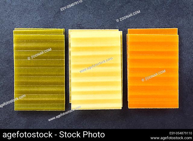 Raw tri color lasagne pasta sheets, photographed overhead on slate