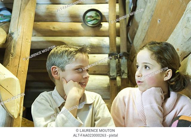 Preteen boy and girl sitting side by side, talking
