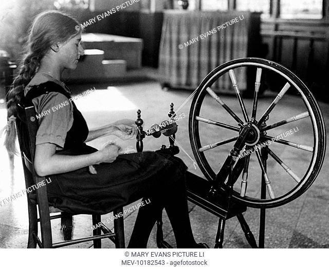 Teenage girl with her hair in a plait, using a spinning wheel