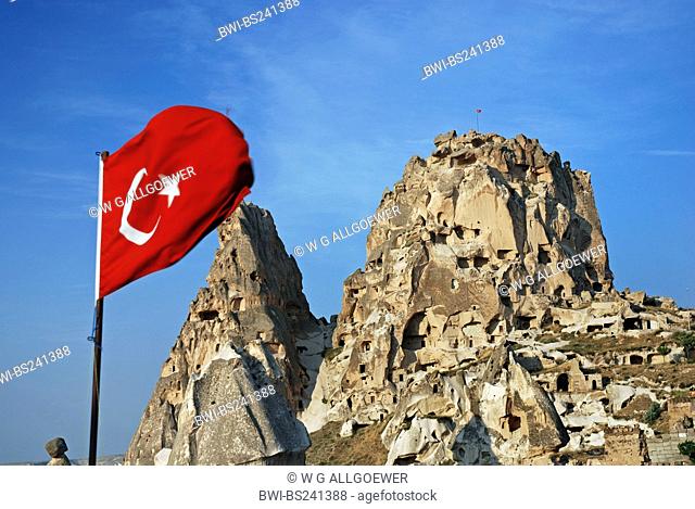 historical cave architecture built into tuff formations with the turkish flag waving in the foreground, Turkey, Cappadocia, Uchisar