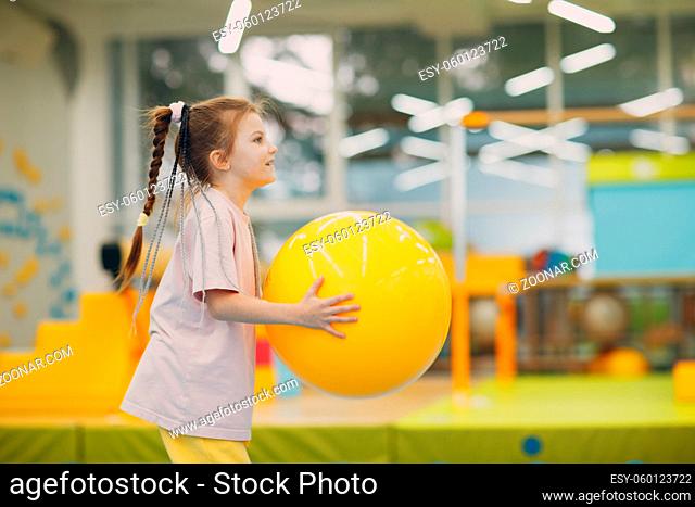 Little girl playing and doing exercises with big yellow ball in gym at kindergarten or elementary school. Children sport and fitness concept