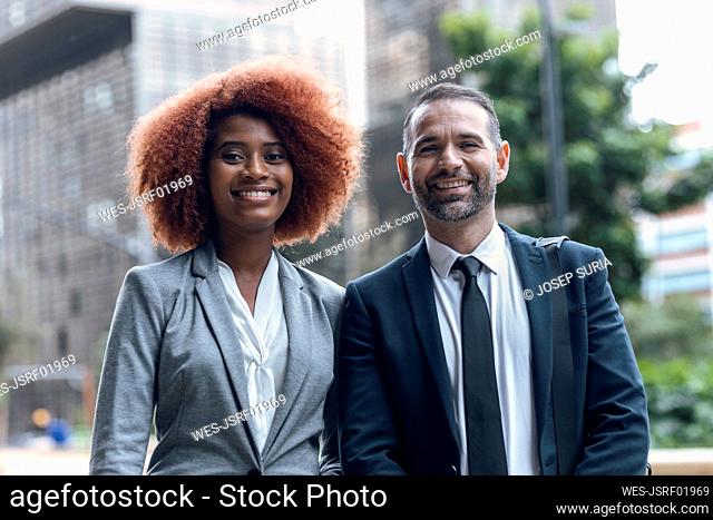 Portrait of two business colleagues standing side by side and smiling at camera