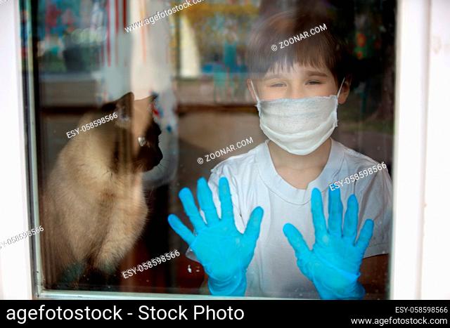 Quarantine from a child of COVID-19. American boy in a mask outside the window