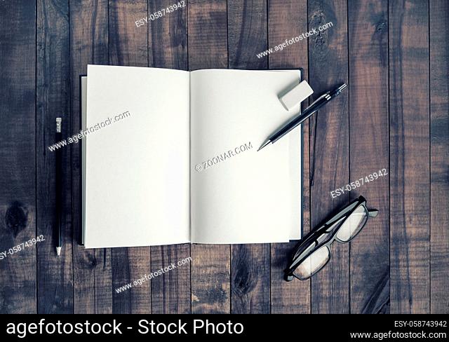 Opened blank notebook, glasses, pencil and eraser. Stationery on vintage wood table background. Flat lay
