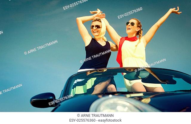 Zwei Frauen in Cabrio genießen einen Auto Ausflug im Sommer und strecken die Arme aus