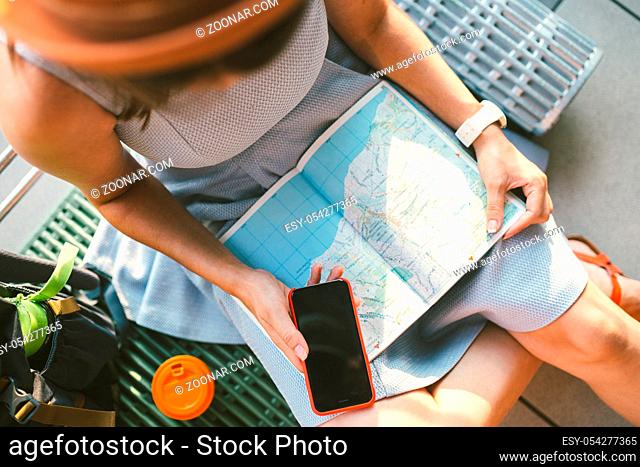 Theme travel planning. The top view hands Caucasian woman uses smart phone and studies the tourist map, passes route, navigates through the paper map