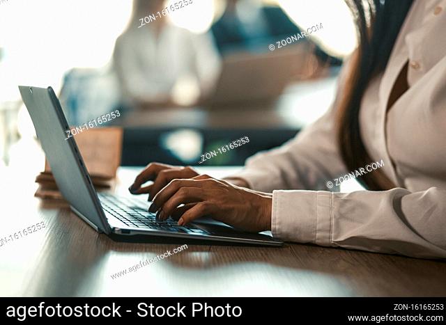 Office manager typing laptop keyboard. Coworkers working in office on blurred background. Toned image. Close up shot of female hands