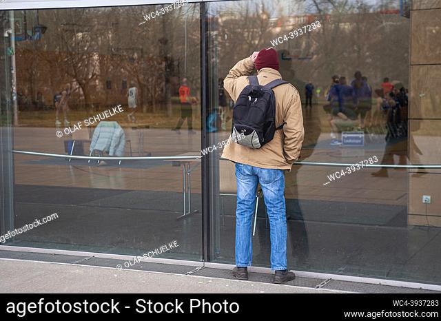 Berlin, Germany, Europe - A man stands close to a pane of glass and watches a basketball game from outside the Max-Schmeling-Halle arena in Prenzlauer Berg in...