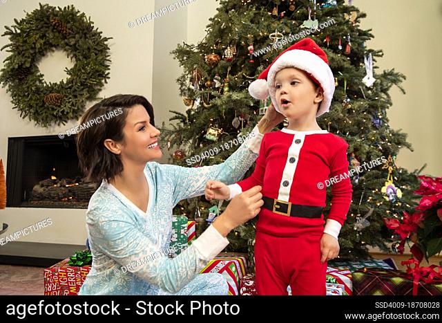 Young boy and his mother in pajamas gathered around Christmas tree