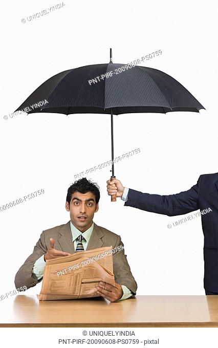 Businessman reading a newspaper under umbrella
