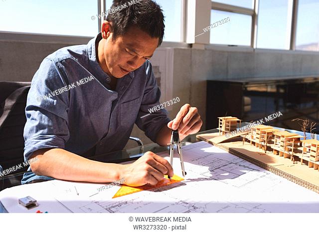 Male architect working on blueprint at desk in a modern office