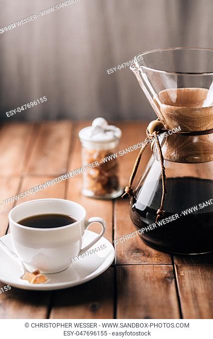 A tabletop scene with coffee, more coffee running through a coffee maker and some rock candy on a wooden table