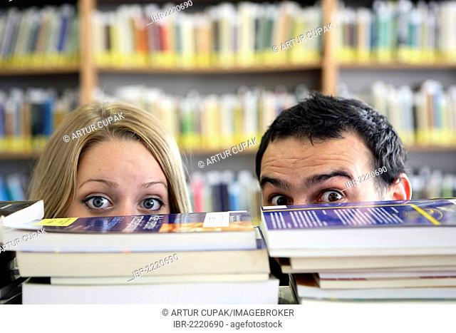 Students, pair, looking out from behind stacks of books, university library