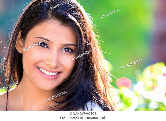 Closeup headshot portrait of confident smiling happy pretty young woman, isolated background of blurred trees, flowers. Positive human emotion facial expression...