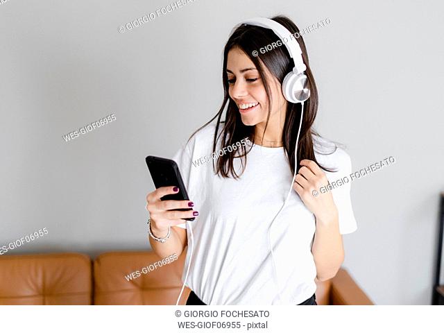 Happy young woman with smartphone and headphones at home