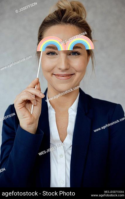 Smiling businesswoman holding rainbow prop at office