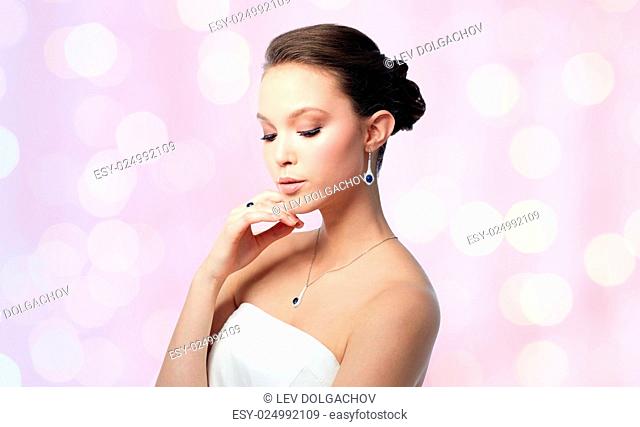 beauty, jewelry, people and luxury concept - beautiful asian woman or bride with earring, finger ring and pendant over rose quartz and serenity lights...