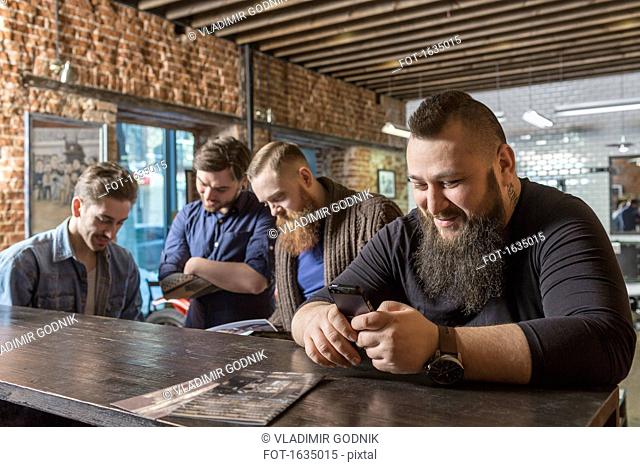 Male hairdresser using mobile with coworkers at bar counter in barber shop