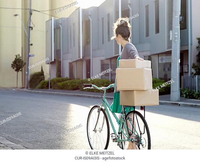 Young woman pushing bicycle with cardboard boxes