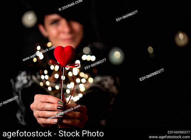 The girl holds red heart in hand on a garland bokeh background