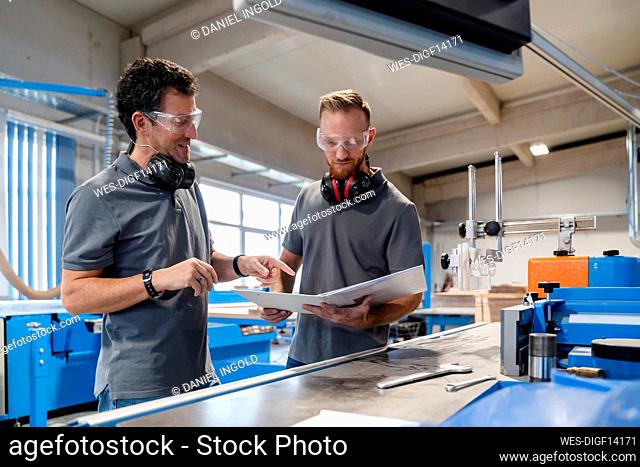 Two male carpenters talking over documents in production hall
