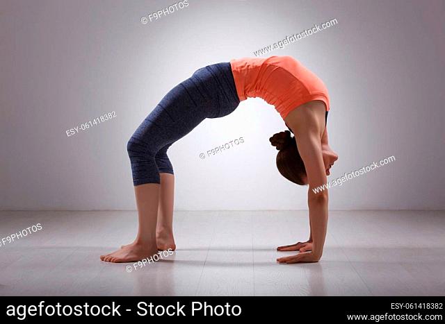 Beautiful sporty fit yogini woman practices yoga asana chakrasana (or urdva dhanurasana) - wheel pose (or upward facing bow) pose in studio